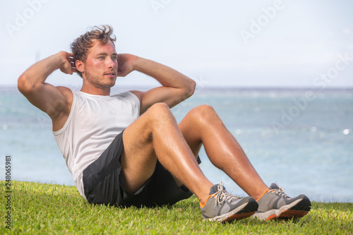 Fit man athlete training outside on grass doing situps for abs workout fat belly weight loss. Healthy active lifestyle.