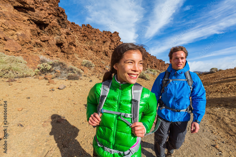 Happy hikers on mountain climb hike trekking with cold jackets and  backpacks healthy active lifestyle. Young Asian woman with Caucasian man  smiling walking outdoors. Stock Photo