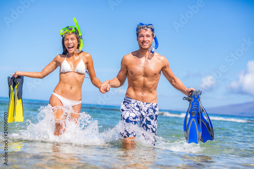 Happy summer fun couple on beach vacation swimming with snorkel equipment running in ocean water. Excited Asian bikini woman and Caucasian man on tropical holidays with flippers and mask. photo