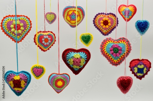 Knitted hearts of colored yarn hang on threads on a white background. Valentine's Day, love, handmade, amigurumi, hobby, decoration, postcard, creative.