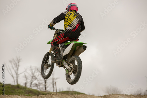 Fototapeta Naklejka Na Ścianę i Meble -  Racer on motorcycle participates in motocross cross-country in flight, jumps and takes off on springboard against sky. Concept active extreme rest.