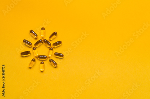 Close up capsules of fish fat oil in the sun shape, omega 3, vitamin e on the yellow background. Healthy food diet. Nutritional supplement photo