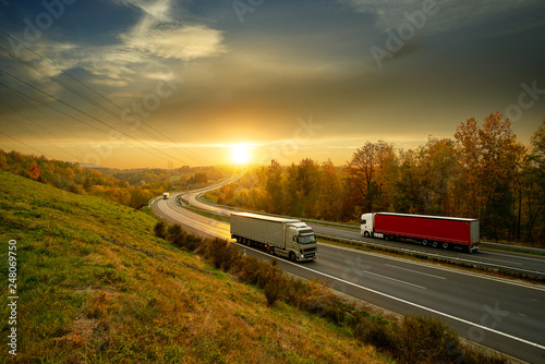 Obraz na płótnie Passing trucks on the asphalt highway in autumn landscape at sunset w salonie