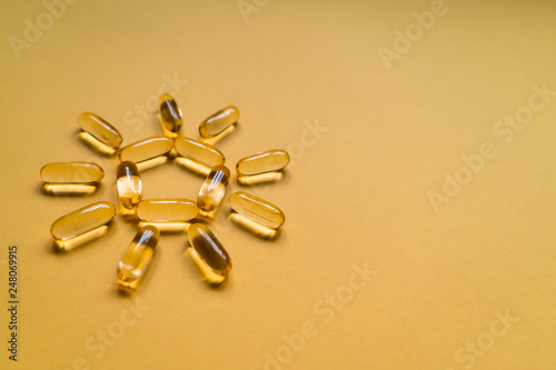 Close up capsules of fish fat oil in the sun shape, omega 3, vitamin e isolated on yellow background. Healthy food diet. Nutritional supplement