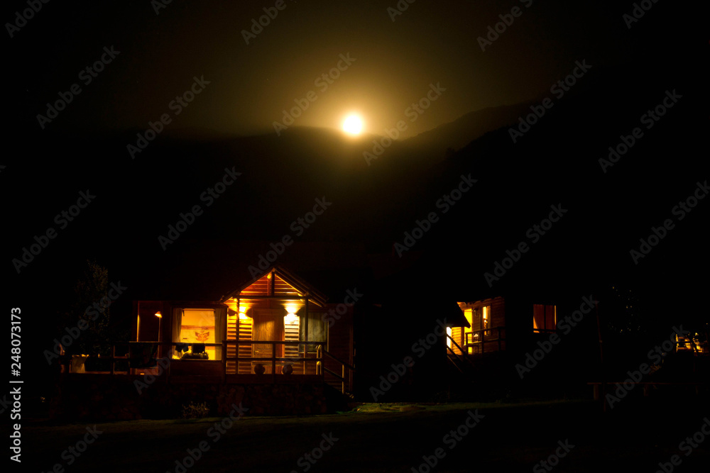 night sunset in the mountains. the moon sets behind the mountains. foreground houses with lanterns