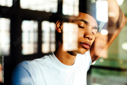 Portrait of a young man with eyes closed, standing against large windows