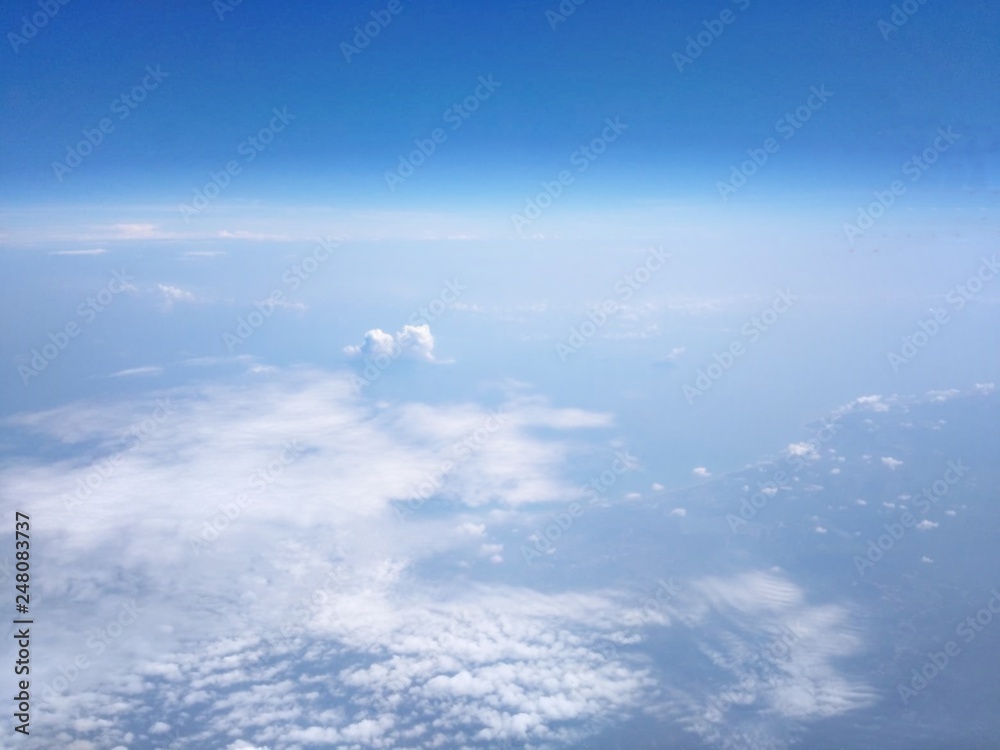 View from the high angle of the sky, clouds, fluffy, soft, space with shades of blue sky and earth background from above flying airplane window in bright morning sunrise View from the high angle of the sky, clouds, fluffy, soft, space with shades of blue sky and earth background from above flying airplane window in bright morning sunrise