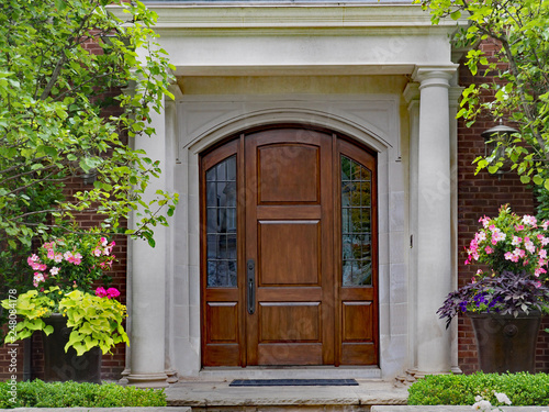 elegant wooden front door and portico entrance surrounded by flowers of upper class house
