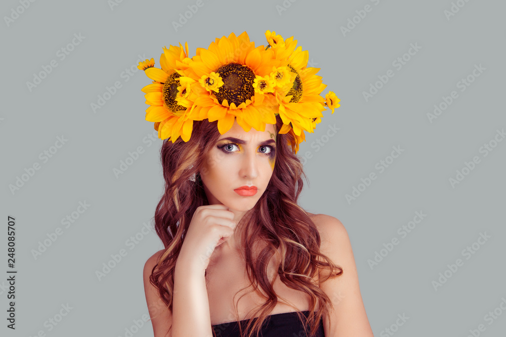 Upset woman with floral headband looking at you camera frustrated fist, hand on chin thoughtful isolated on gray background. Fashion beauty girl with crown from sunflowers on head Upset woman with floral headband looking at you camera frustrated fist, hand on chin thoughtful isolated on gray background. Fashion beauty girl with crown from sunflowers on head