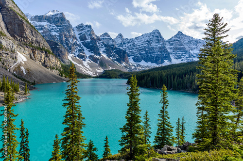 Moraine Lake - A panoramic sunny Spring evening view of emerald-color Moraine Lake surrounded by pine forest and rugged high peaks at Valley of the Ten Peaks of Banff National Park, AB, Canada.