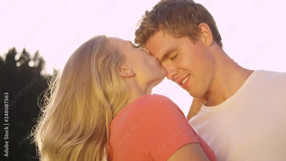 SLOW MOTION, CLOSE UP, LENS FLARE: Happy man and woman kiss each other on the forehead on a romantic summer day. Golden sun rays shining on the happy couple enjoying their date in nature and kissing. SLOW MOTION, CLOSE UP, LENS FLARE: Happy man and woman kiss each other on the forehead on a romantic summer day. Golden sun rays shining on the happy couple enjoying their date in nature and kissing.