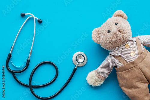 Children's doctor concept. Teddy bear toy and stethoscope on blue background top view space for text
