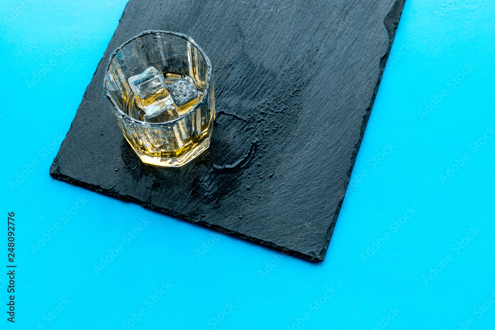 In the bar. Whiskey with ice on black desk on blue background top view space for text