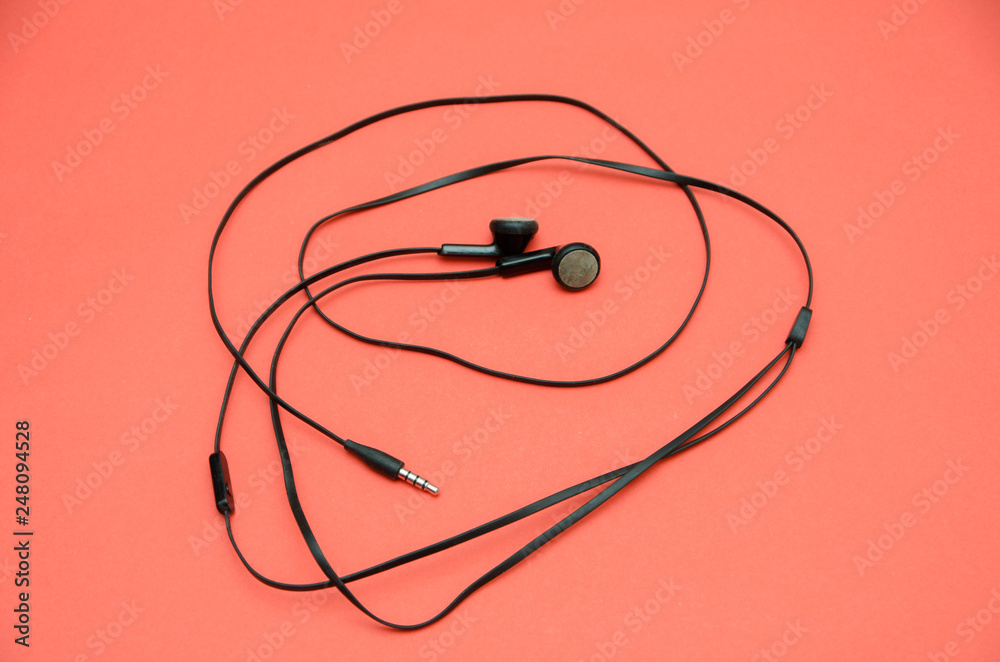 Beautiful modern, digital, plastic, vacuum, black headphones with wires for listening to music on a purple-pink background Beautiful modern, digital, plastic, vacuum, black headphones with wires for listening to music on a purple-pink background