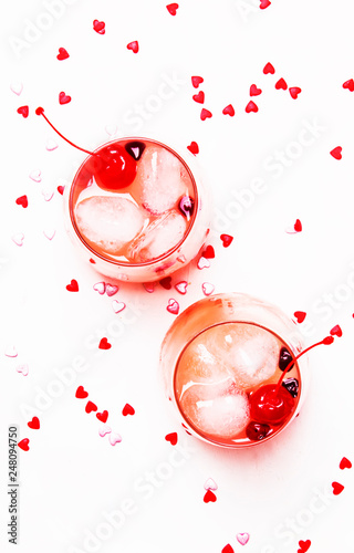 Pink alcoholic cocktail for Valentines day, two glasses, white background with sweet hearts, top view