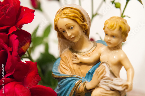 A statue of the Virgin Mary with Baby Jesus in her arms next to a bouquet of roses in a chapel.