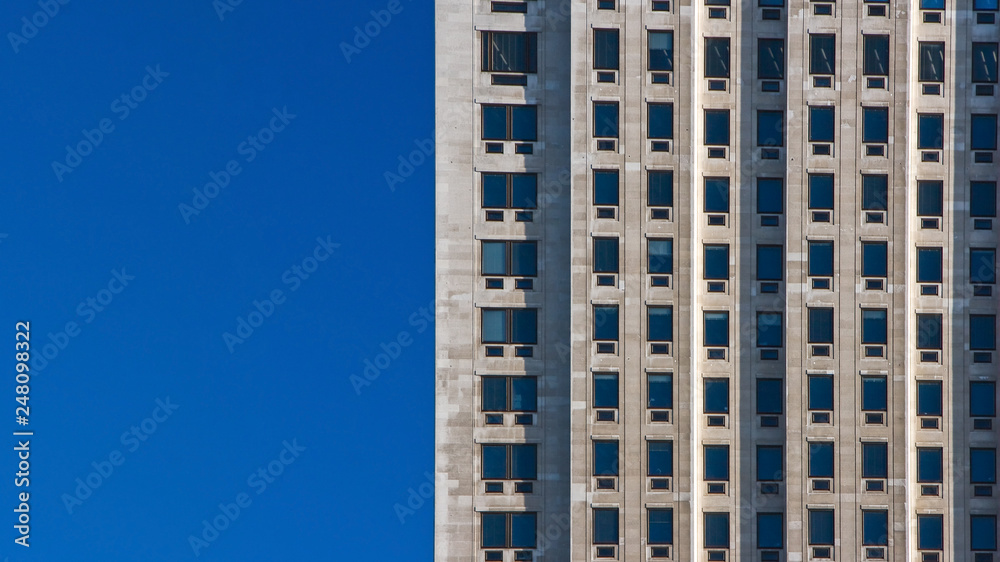 Regular pattern made of rectangular windows on block of flats / offices building. Clear sky (place for text) on left side.