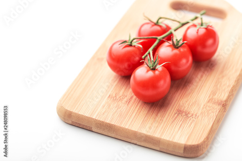 A branch of cherry tomatoes lies on a rectangular cutting board.