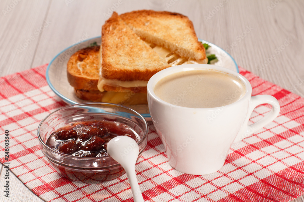 Toasted slices of bread with cheese on white plate, cup of coffee, bowl with strawberry jam and spoon on napkin. Toasted slices of bread with cheese on white plate, cup of coffee, bowl with strawberry jam and spoon on napkin.