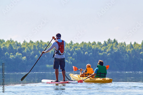 Man on stand-up paddle board SUP and people in yellow kayak paddling at the morning at Danube river