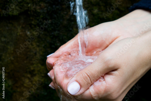 water flows into women's hands, hands with splashes of water, pure spring water