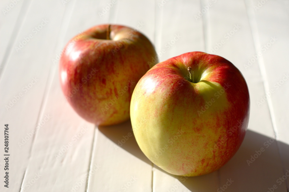 Two jonagold apples in the sun on a white table