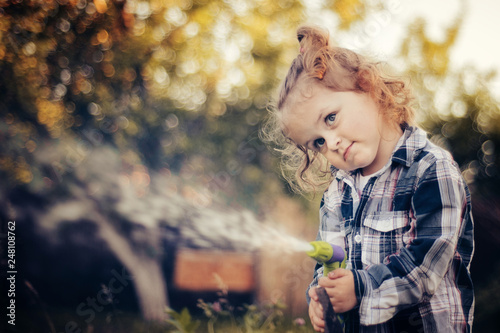 Young cute girl spraying water with a hose