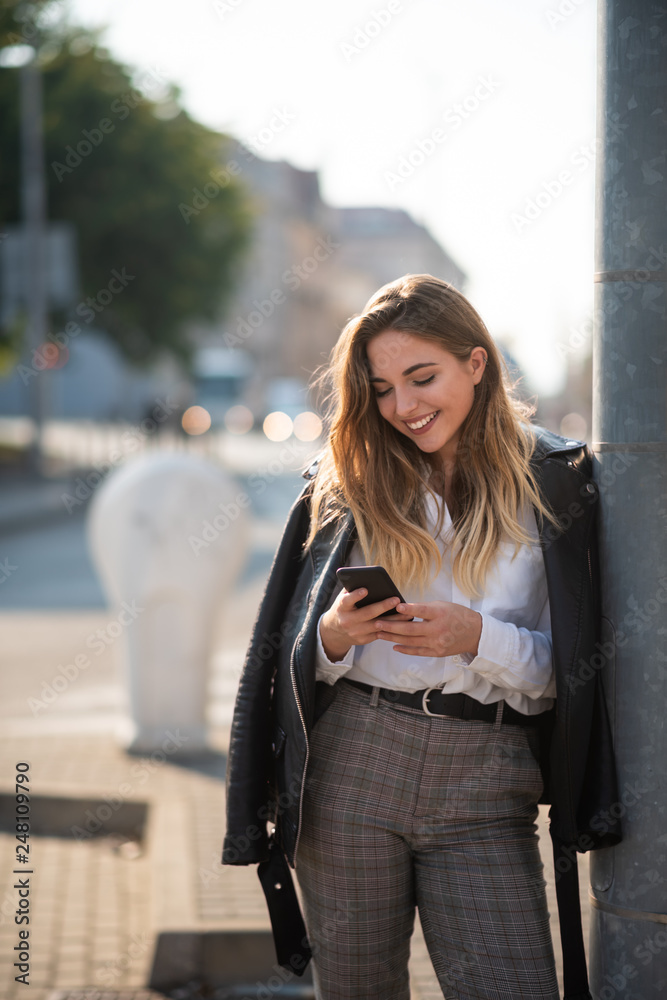 Woman with smartphone leaning against light post Woman with smartphone leaning against light post