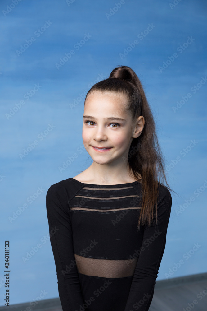Portrait of a beautiful little brown-haired girl smiling on a blue background. Dressed in a black sweater, hair collected in a ponytail. Portrait of a beautiful little brown-haired girl smiling on a blue background. Dressed in a black sweater, hair collected in a ponytail.