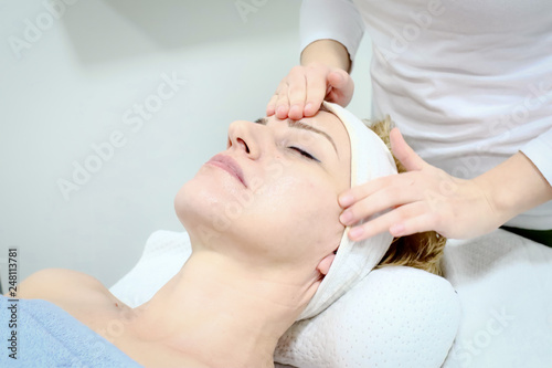 beautician worker gently massages face of  female costumer in beauty salon