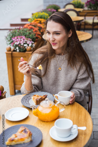 Young attractive smiling woman in gray knitted sweater drinking tea outdoors at the street cafe. © Anna