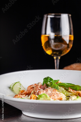 Concept of Italian cuisine. Caesar salad with salmon, lettuce mix, cherry and parmesan cheese. A glass of white wine on the table. Serving dishes in the restaurant. copy space