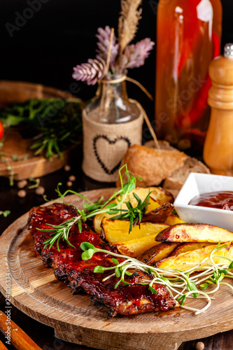 Grilled ribs with potatoes in a rustic style with barbecue sauce. Serving dishes in the restaurant on a wooden board. A glass of cool wine. Background image close up. copy space