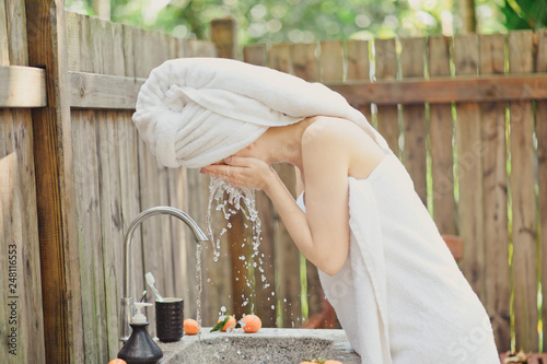 Portrait of beautiful young woman washing her face splashing water in outdoor bathroom
