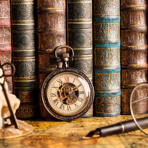 Antique clock on the background of a candle with a key and books. Vintage style. 1565 old map of the year.