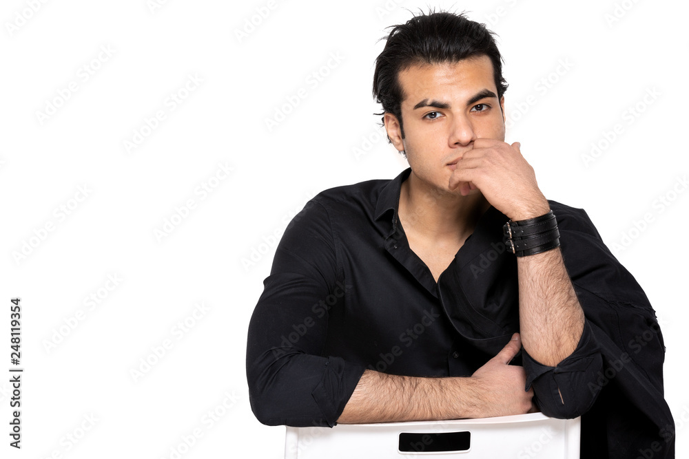 dark-haired young man thoughtfully sitting on a chair on an isolated background dark-haired young man thoughtfully sitting on a chair on an isolated background