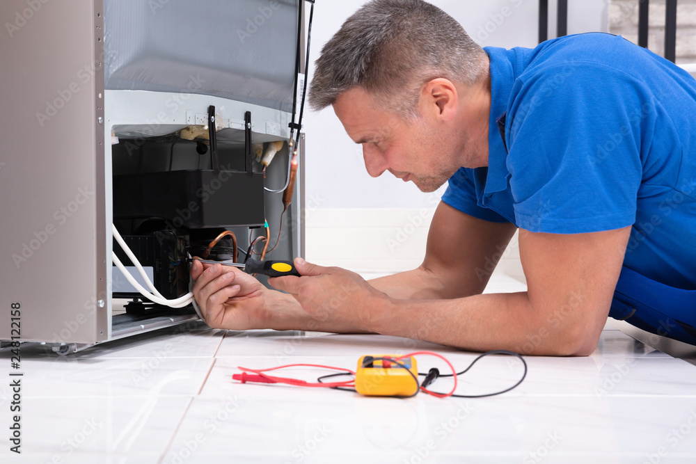 Serviceman In Overall Working On Fridge Serviceman In Overall Working On Fridge