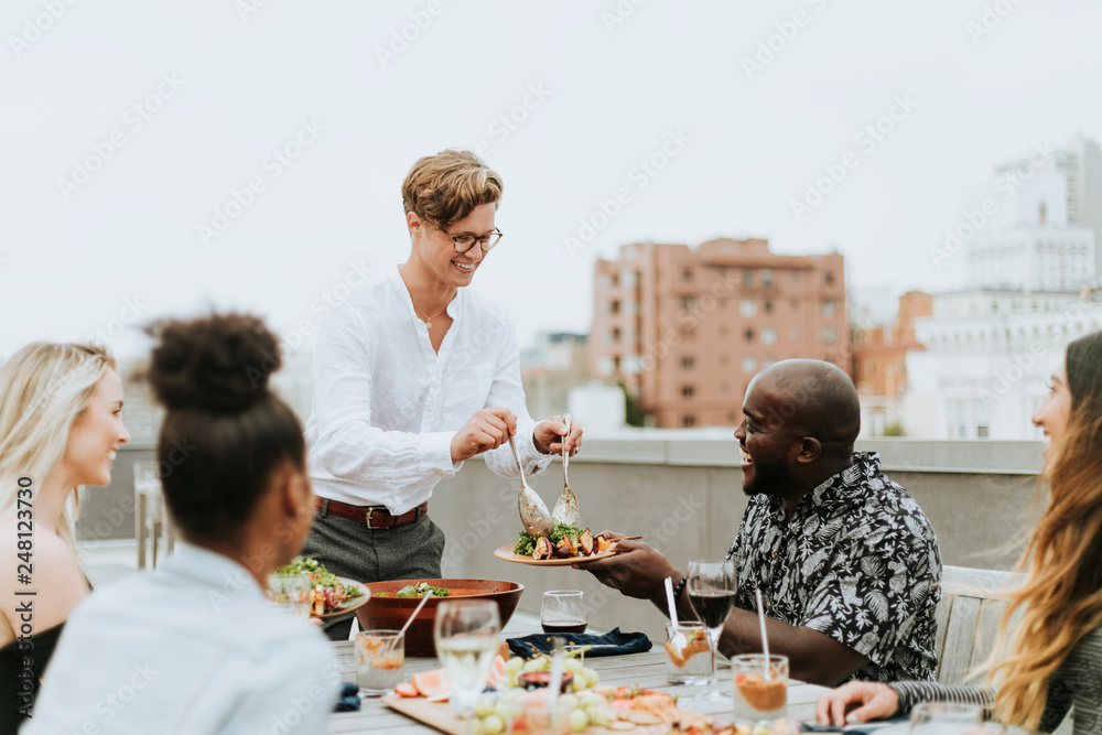 Man serving his friends salad at a rooftop party