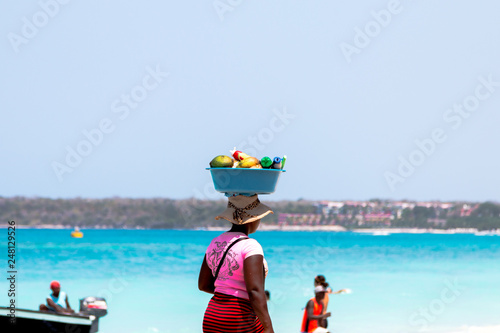 Frau trägt einen Korb mit früchten auf dem Kopf an einem Karibikstrand in Kolumbien