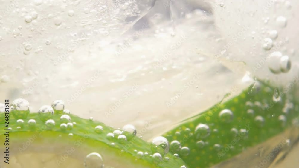 Macro close-up shot of cold refreshing soda tonic fizzy water drink with bubbles interacting with ice and lime