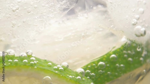 Macro close-up shot of cold refreshing soda tonic fizzy water drink with bubbles interacting with ice and lime