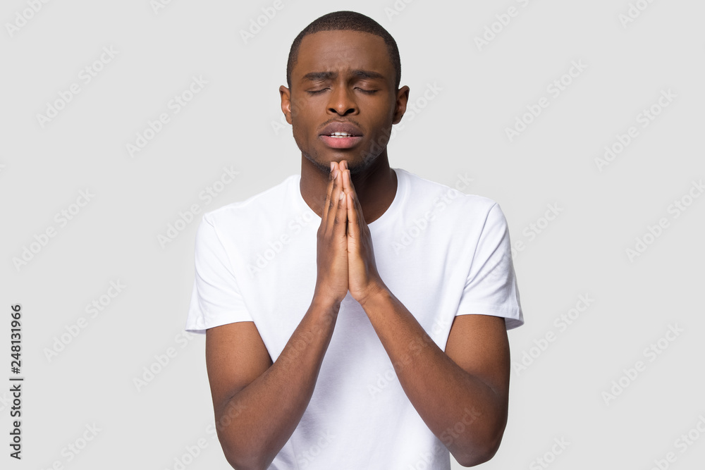 Religious black guy praying with hope isolated on studio background Religious black guy praying with hope isolated on studio background