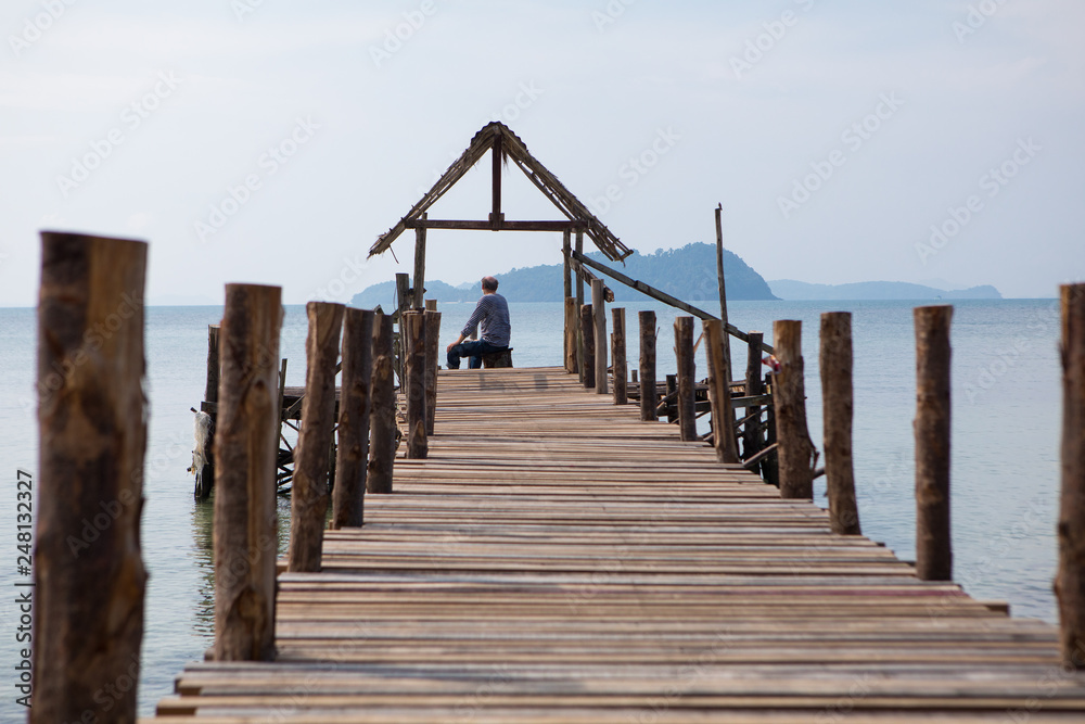 The old man sits on the pier and looks at the sea, the view from the back