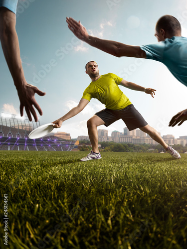 Two team play ultimate frisbee in stadium. One athlete give passes, other players bocked him. Around sunny day