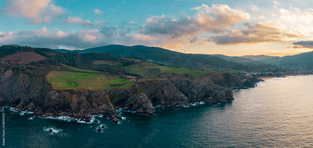 Aerial; view of rocky shore with a rough sea; steep dangerous Bakio bank with countryside life; bright evergreen field and picturesque sunset in winter evening; landscapes of northern coast of Spain