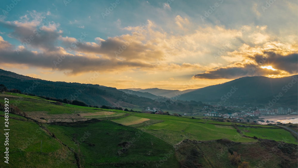 Aerial rural view of green fields and little villages on the hills; northen part of Spain; winter cloudy weather, evergreen plants and trees; fresh sea air, sun shining throug the dramatic sky, Bakio