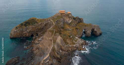 Aerial drone view of islet on the coast of Biscay with hermitage on the top; small church on the stone island, steep slope and rough coast in this area; craggy rocky uninhabited isle with old history photo