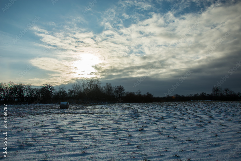The sun setting behind the cloud and snow in the field
