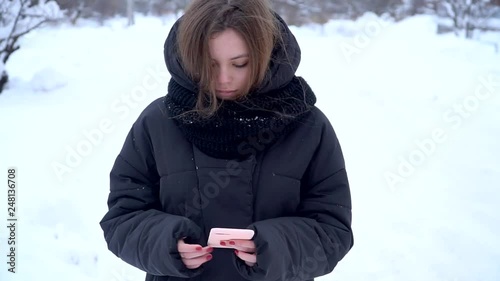 Pretty caucasuian girl teenager using phone outside in winter without grloves social media concept blogger slow motion photo