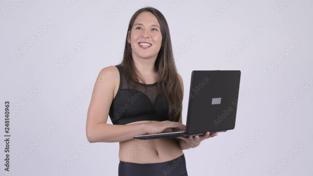 Young happy multi-ethnic woman thinking while using laptop ready for gym Young happy multi-ethnic woman thinking while using laptop ready for gym